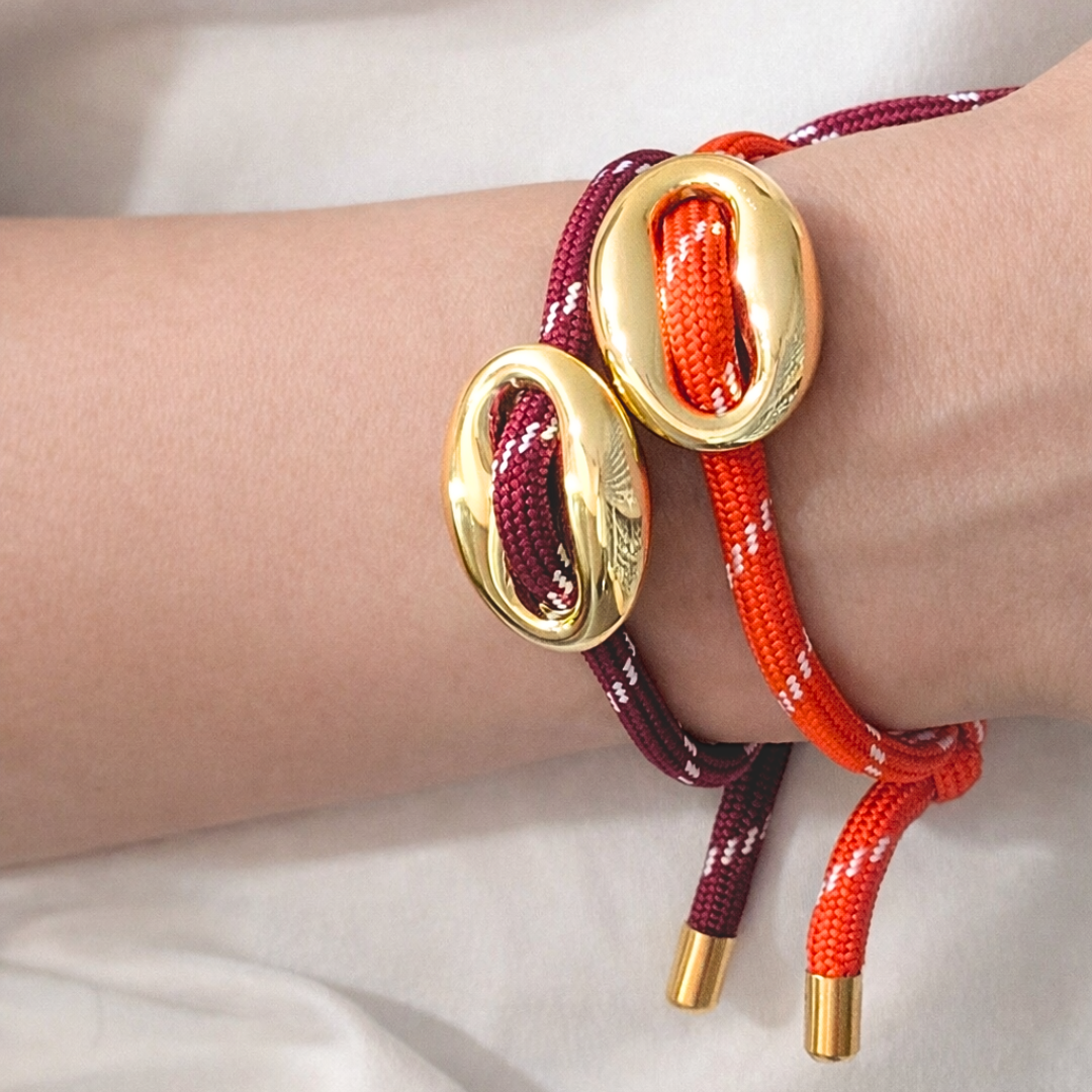 Gouden varkensneus armband van Casa Jadel gedragen om de pols, met verstelbaar touwkoord in burgundy en rood