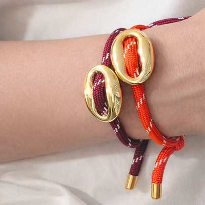 Gouden varkensneus armband van Casa Jadel gedragen om de pols, met verstelbaar touwkoord in burgundy en rood