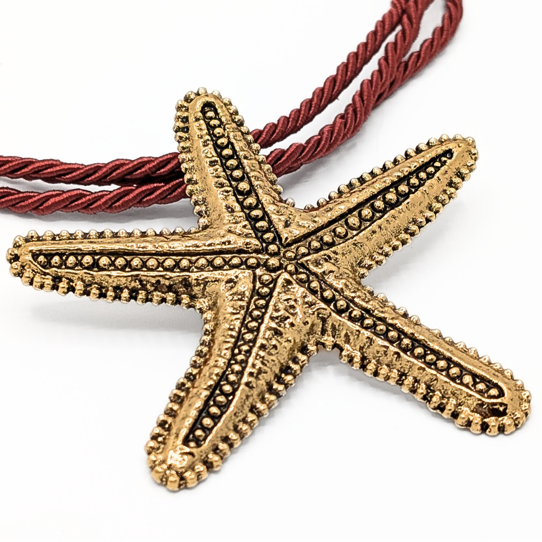 Close-up van grote gouden zeester hanger aan rode rope ketting