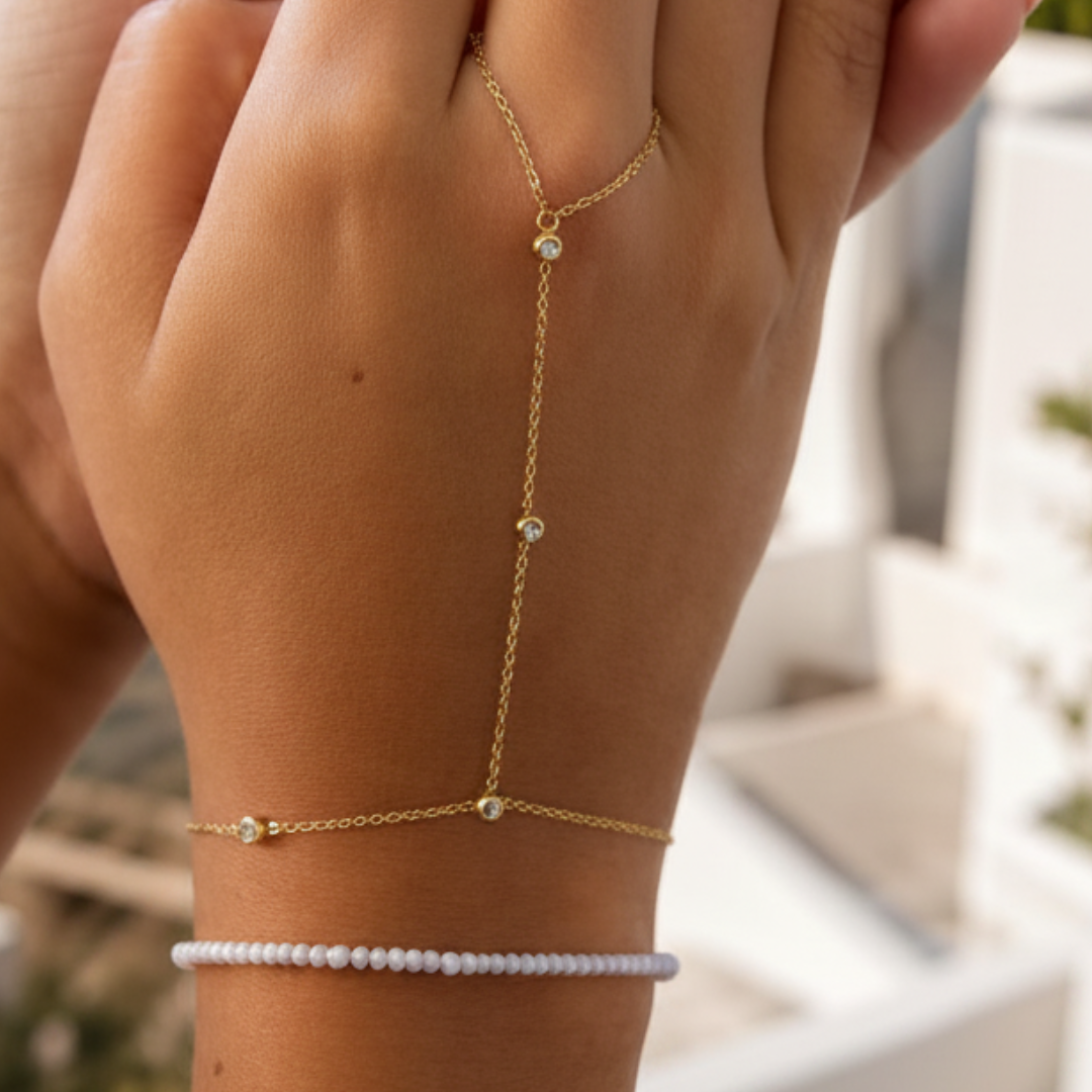 hand met gouden handchain met strass en witte saar armband