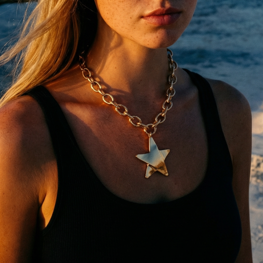 Goudkleurige schakelketting met grote stervormige hanger, gedragen op een zwarte top bij zee tijdens golden hour – stijlvolle statement ketting met Ibiza vibe