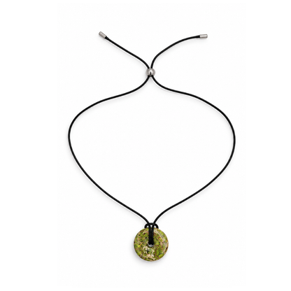 Overzicht van de zwarte koordketting met groene ronde statement hanger en zilverkleurige schuifkraal op een witte achtergrond.