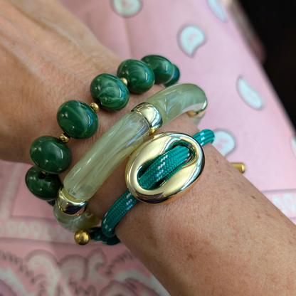 Arm met groene grote kralenarmband met gouden details en een grote tube armband en een rope armband met gouden varkensneus