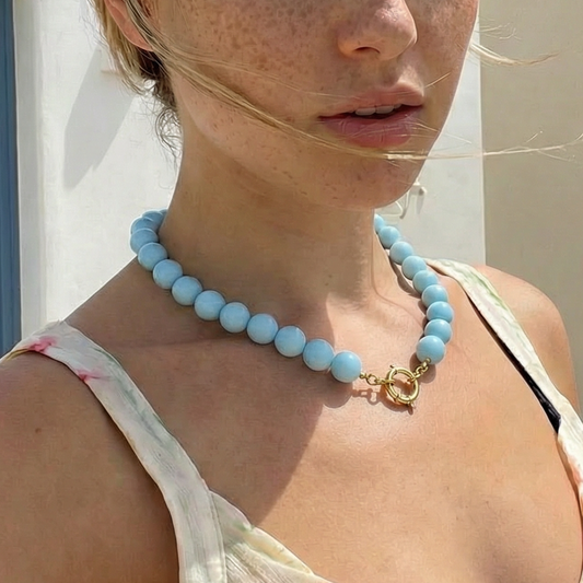 Model draagt grote kralenketting in lichtblauw met boeislot.