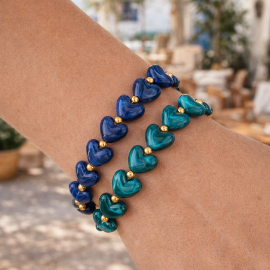 Pols met blauwe en turquoise hartjesarmbanden met goudkleurige details op een zonnig terras in Ibiza stijl