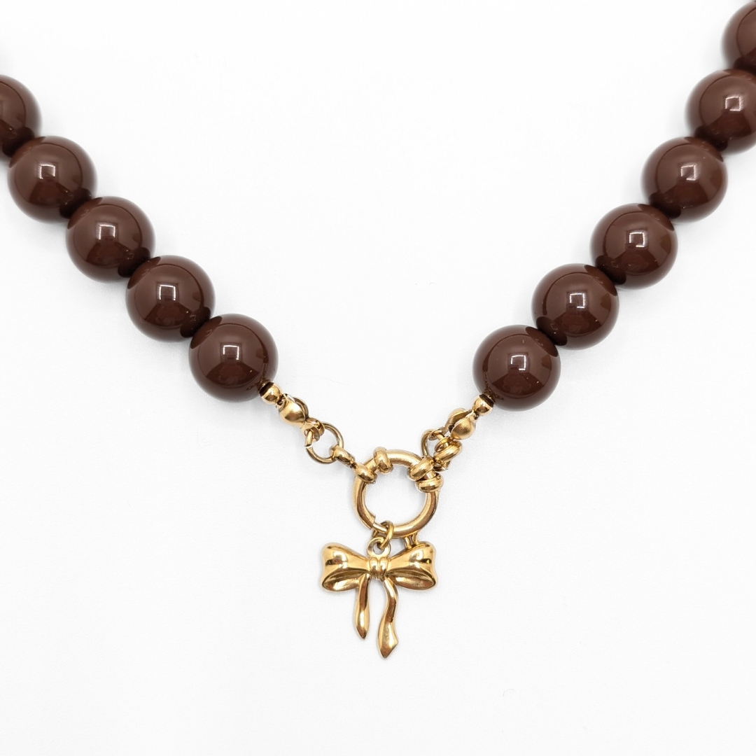Ingezoomd chocoladebruine kralenketting met goudkleurige strikbedel van Casa Jadel