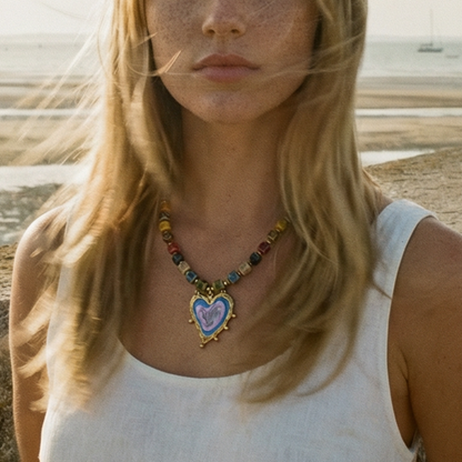 Keramiek kralenketting met multicolor kralen en grote hartvormige hanger, gedragen in een natuurlijke strandsetting – kleurrijke statement ketting met Ibiza vibe
