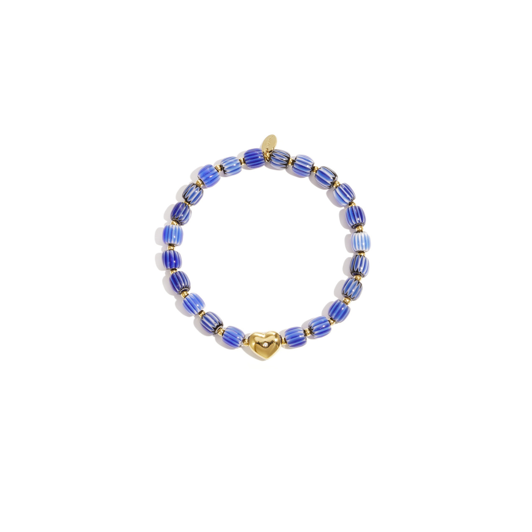 Blauw keramisch armbandje met gestreepte kralen en een goudkleurige hartjes bedel, gefotografeerd op witte achtergrond.