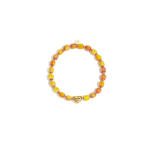 Geel-oranje keramisch armbandje met gestreepte kralen en een goudkleurige hartjes bedel op witte achtergrond.