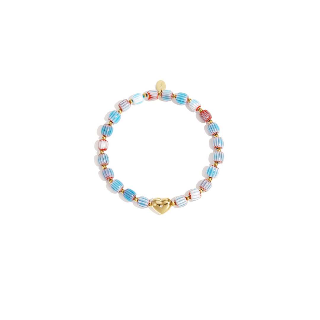 Keramisch gestreept armbandje met roze en witte kralen en een goudkleurige hartjes bedel met strass, gefotografeerd op witte achtergrond.