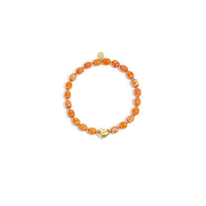 Oranje keramisch armbandje met gestreepte kralen en een goudkleurige hartjes bedel, gefotografeerd op witte achtergrond.