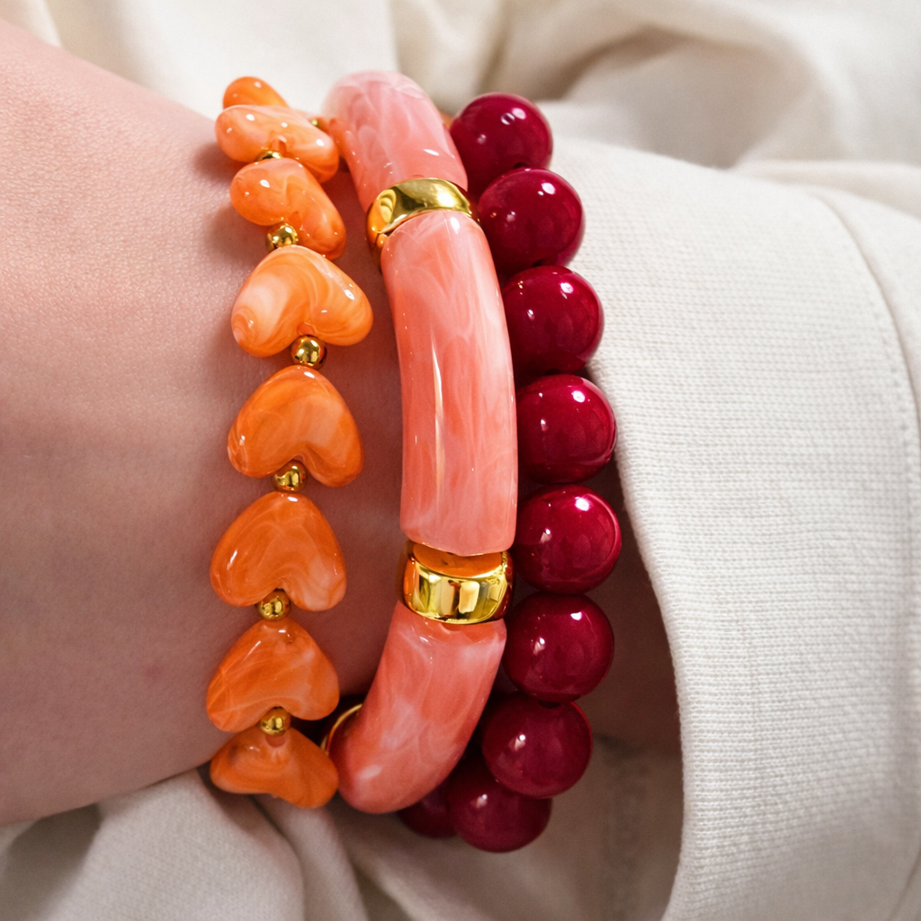 Close-up van kleurrijke armbanden met hartvormige kralen in roze, oranje en bordeaux, gecombineerd met goudkleurige details