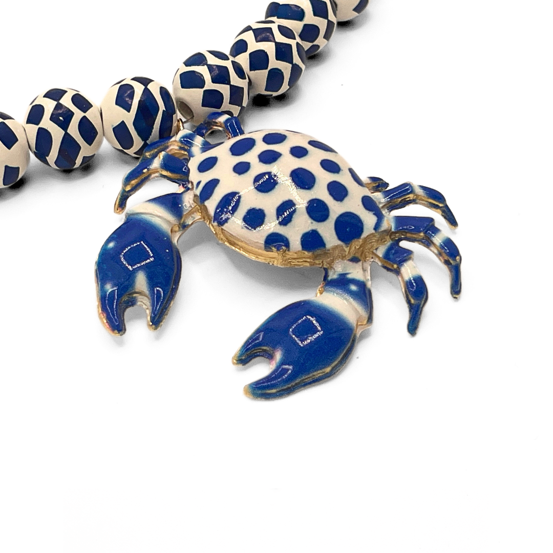 Detail van krab bedel aan wit blauwe kralenketting met speels patroon en zomerse uitstraling