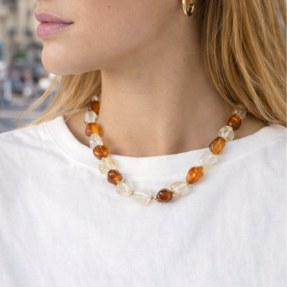 Model kijkt naar rechts en draagt een kralenketting met amber- en ivoorkleurige kralen in een stedelijke setting – Casa Jadel