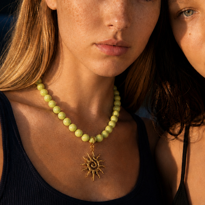 Model draagt een lichtgroene kralenketting met goudkleurige zon bedel van Casa Jadel