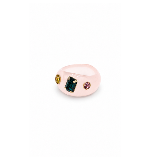 Lichtroze chunky ring met een rechthoekige groene steen, een gele en een roze steentje op een witte achtergrond.