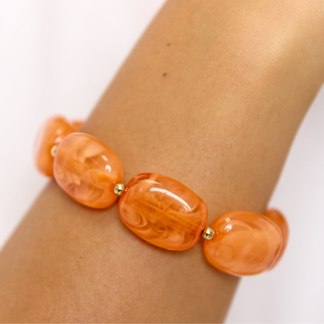 Arm met oranje kralenarmband met marmerlook kralen en gouden accenten 