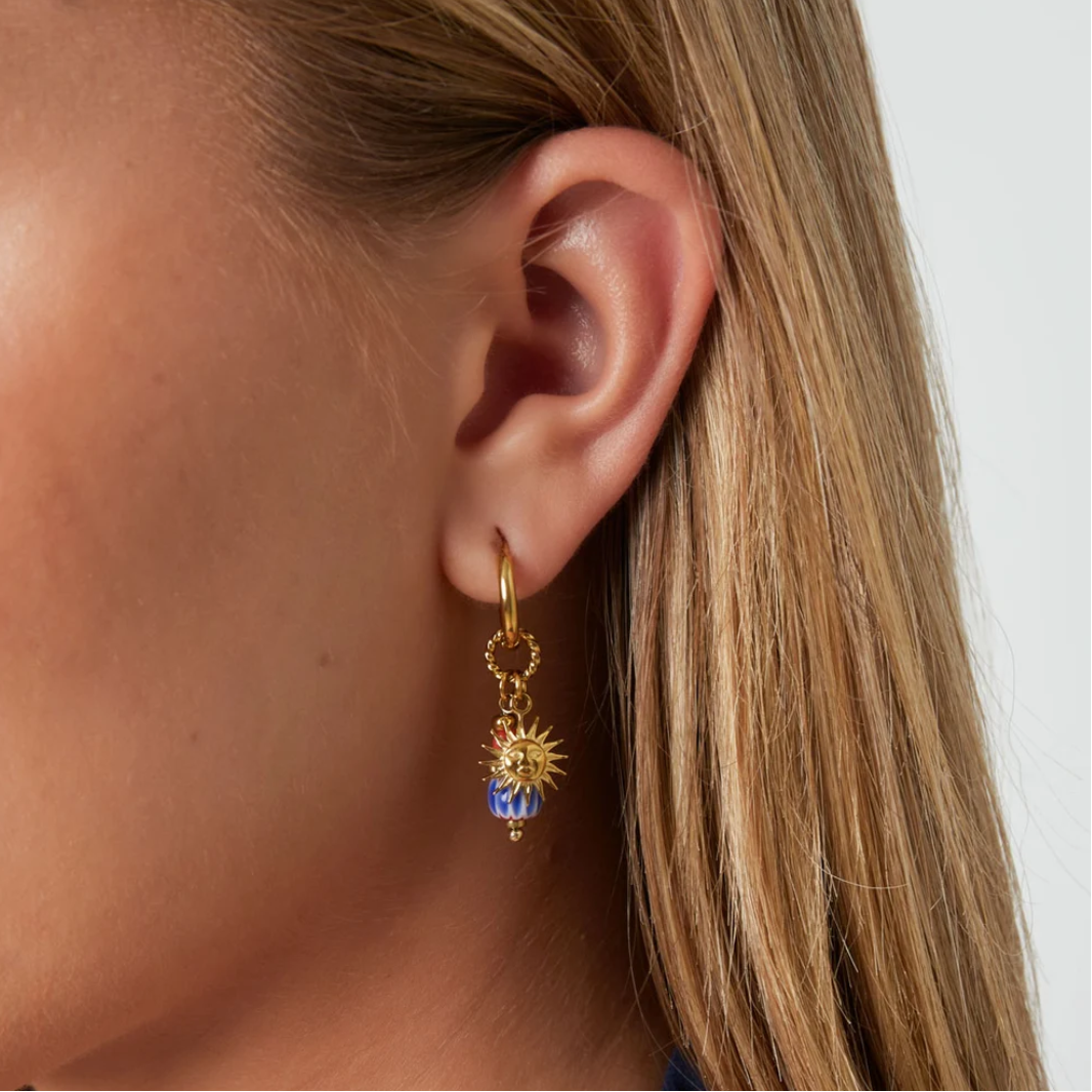 Model met gouden oorbellen met zon bedel en blauwe kraal met oranje detail.