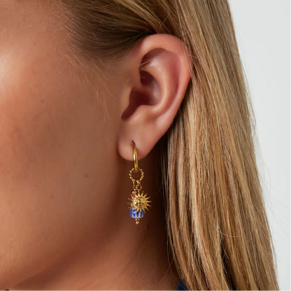 Model met gouden oorbellen met zon bedel en blauwe kraal met oranje detail.