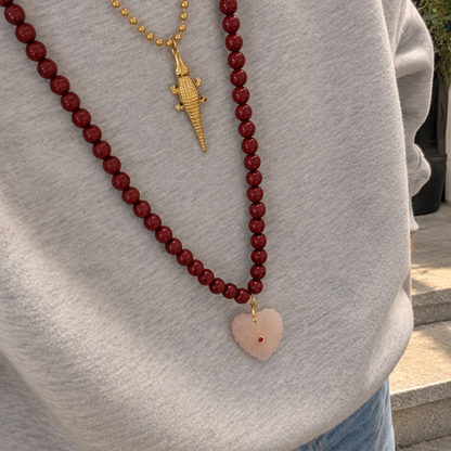 model grijze trui lange burgundy kralenketting met  Rozenkwarts hart natuursteen bedel en gouden ketting met krokodil