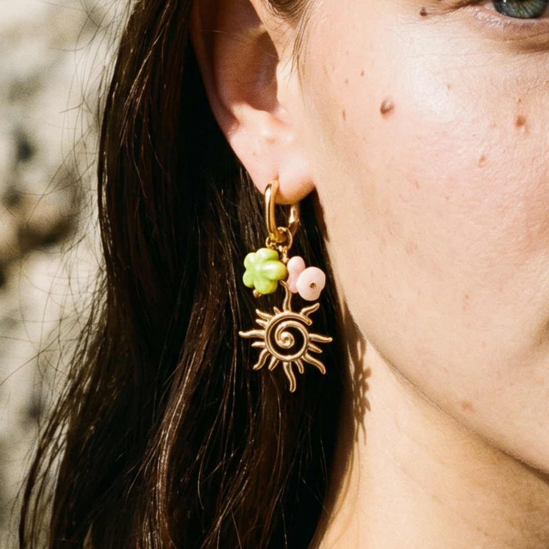 Model draagt gouden oorbellen met zon, natuursteen kraaltjes en groene bloem.