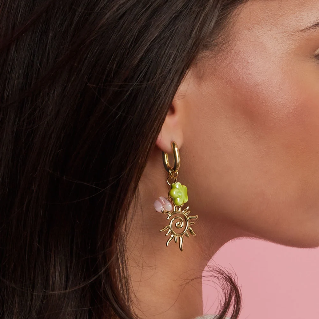 Model met Gouden oorbellen met zon bedel, groene bloem en roze kraal.