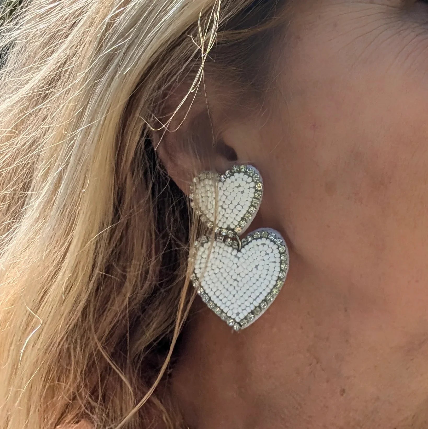 Model met Witte dubbele hart oorbellen met kraaltjes en strassrand op lichte achtergrond.