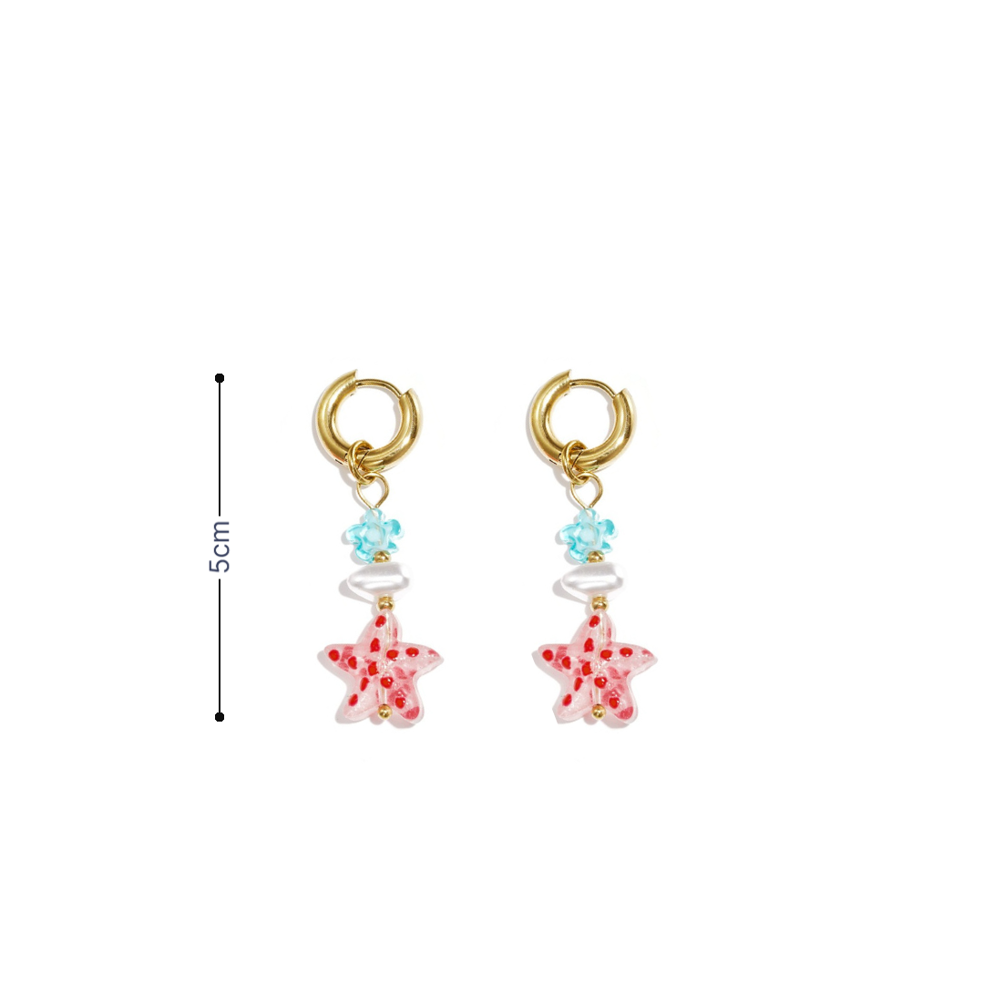 Goudkleurige oorbellen met roze glazen zeester, blauw bloemetje en parelachtige kraal op witte achtergrond met afmeting