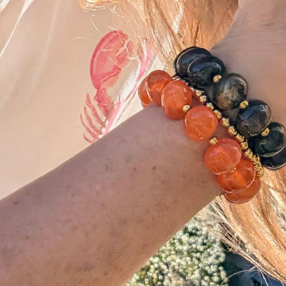 Set van oranje, bruine  en gouden kralenarmbanden met goudkleurige tussenkralen om de pols in zonlicht, Ibiza style sieraden.