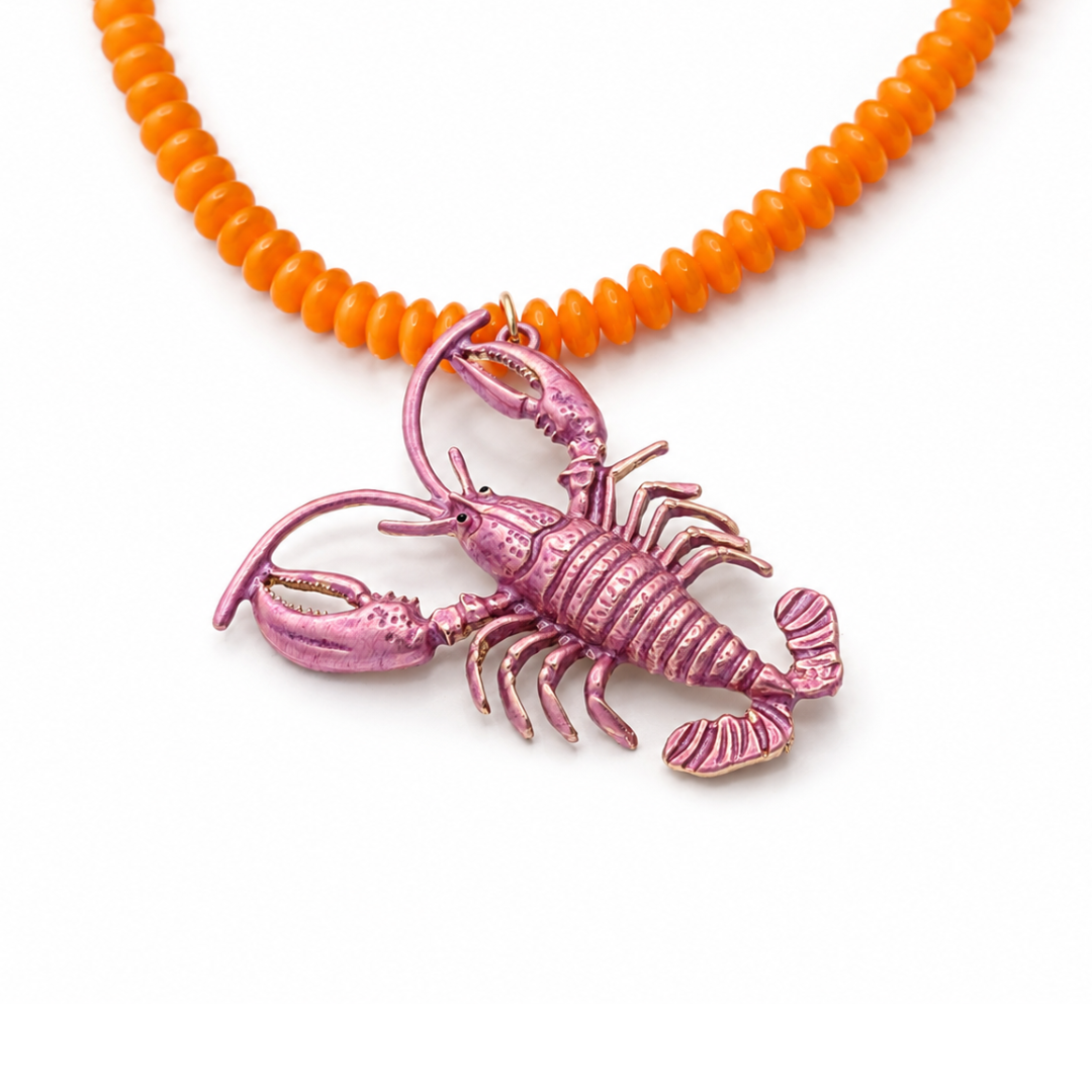 Close up van oranje lange kralenketting met roze metallic kreeft bedel van Casa Jadel. 