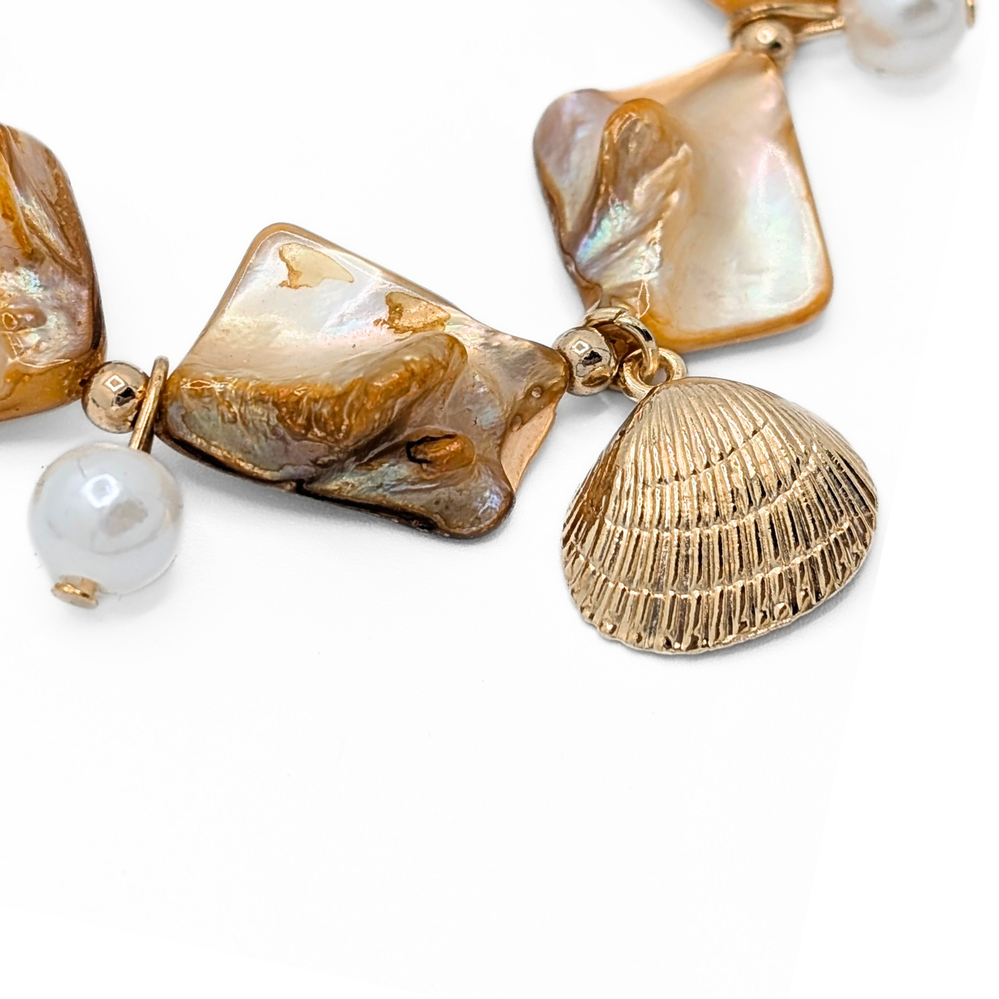 Detail van oranje schelpen armband met gouden schelp bedel en parel