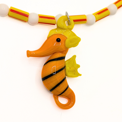 Detail van oranje en witte kralenketting met zeepaardje bedel