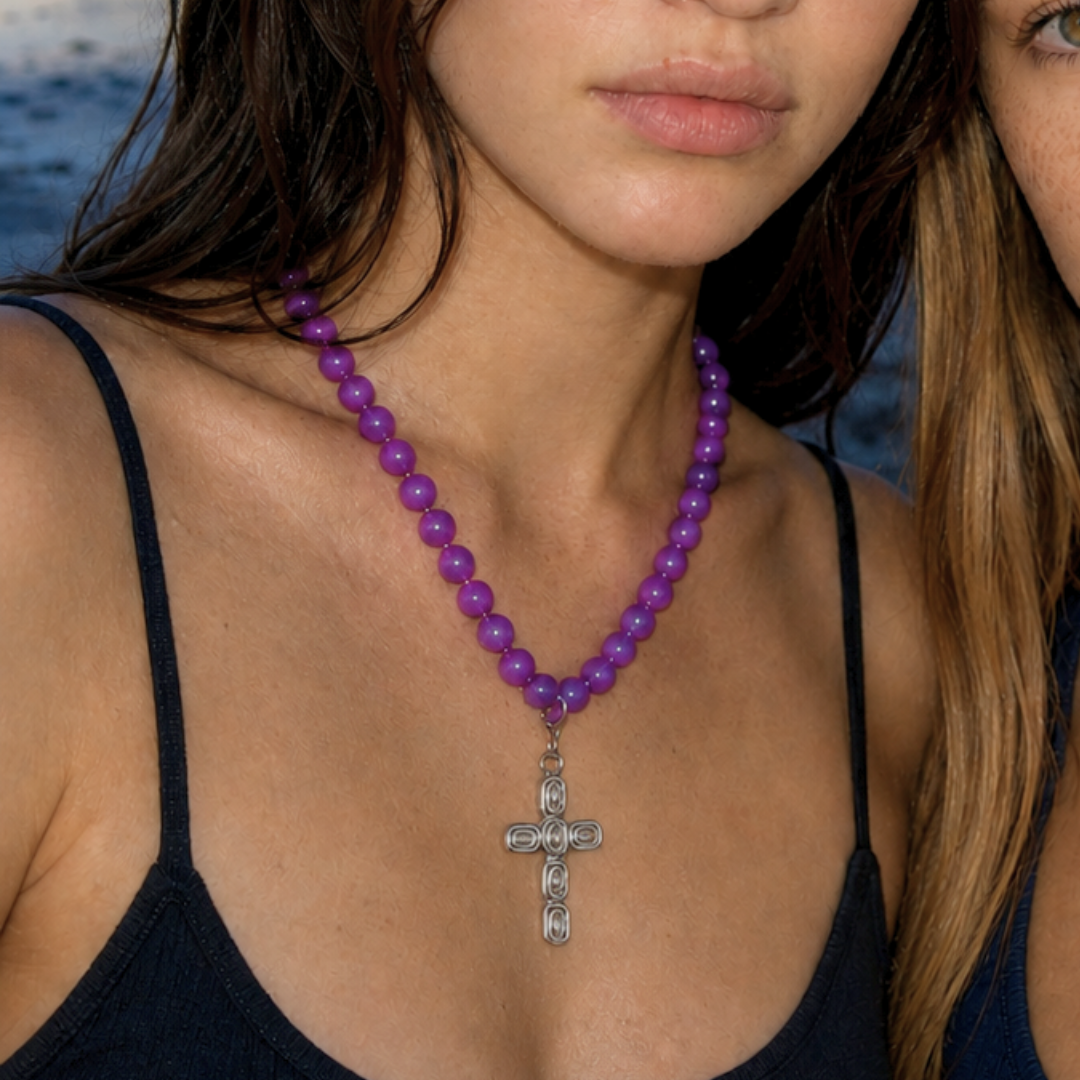 Model draagt een paarse kralenketting met zilverkleurige kruis bedel van Casa Jadel