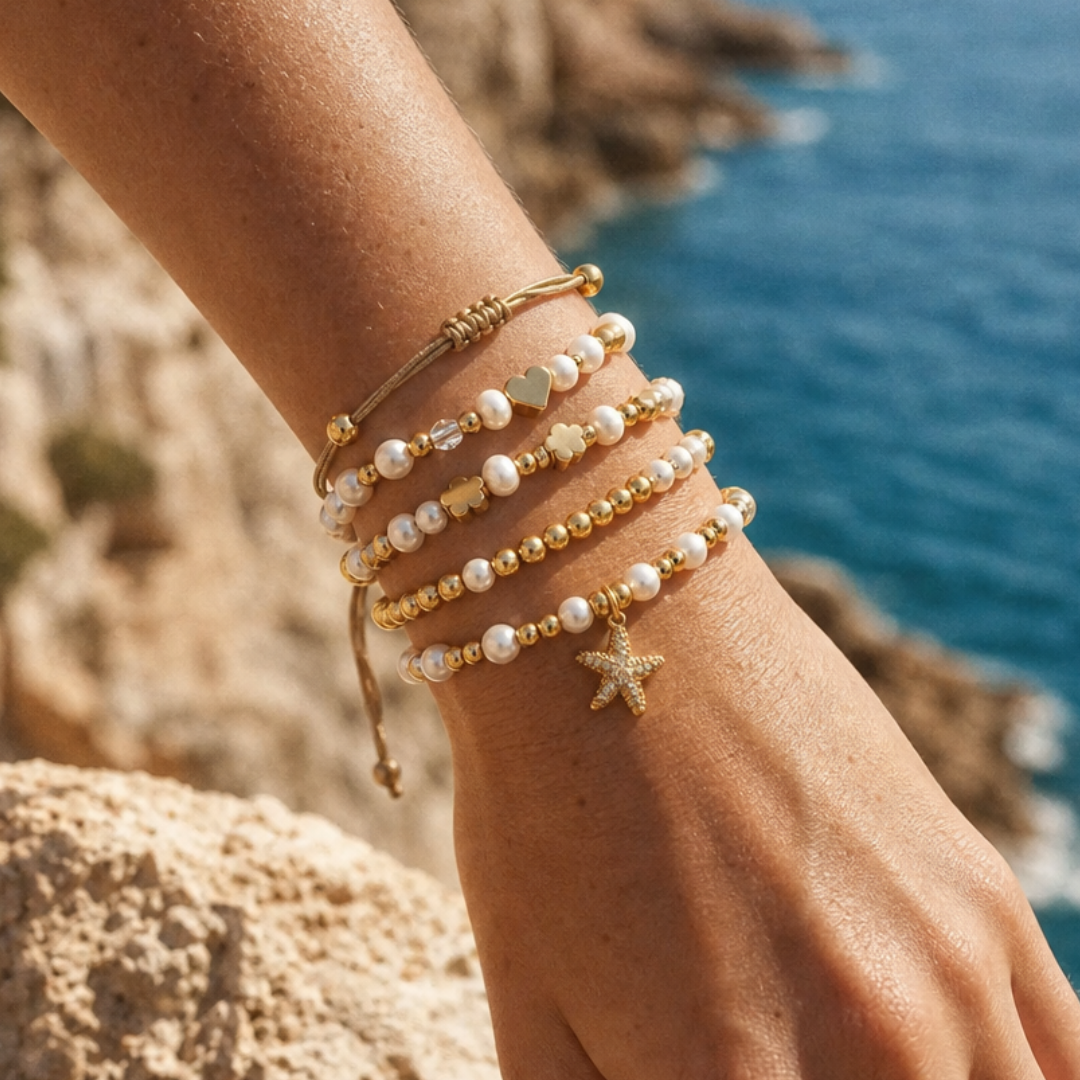 Arm met goudkleurige en parel armbanden stack met hartjes, klavertjes en zeester bedel van Casa Jadel