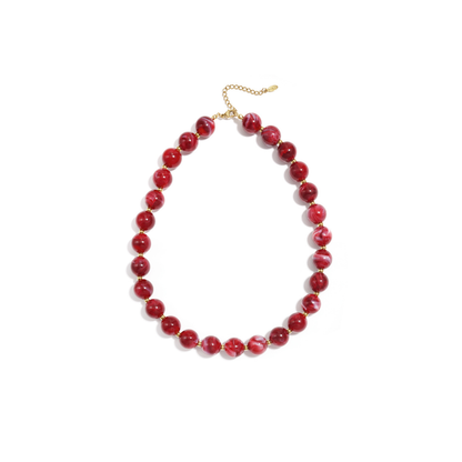 Rode gemarmerde kralenketting met goudkleurige accenten op lichte achtergrond.