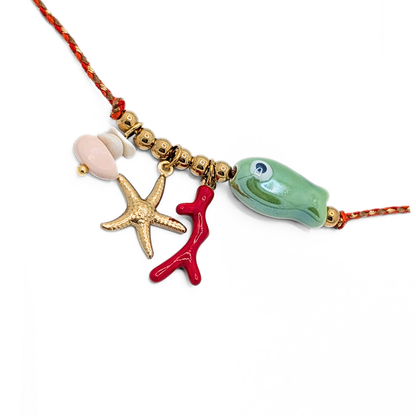 Detail foto van rode rope ketting met goudkleurige kralen en zee bedels zoals zeester, koraal, vis en schelp van Casa Jadel