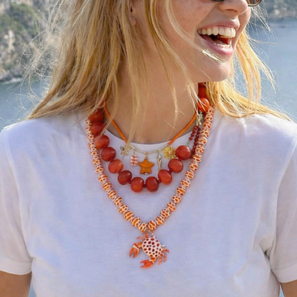 Rood-oranje strand kettingen set met drie lagen en bedels zoals ster zon en krab gedragen op witte top