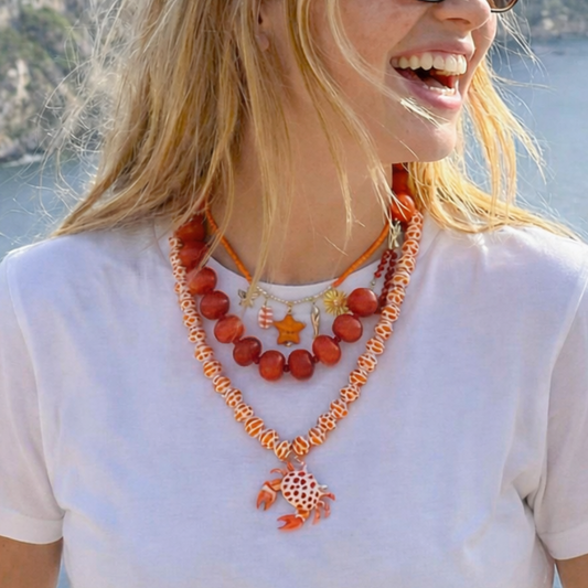 Rood-oranje strand kettingen set met drie lagen en bedels zoals ster zon en krab gedragen op witte top