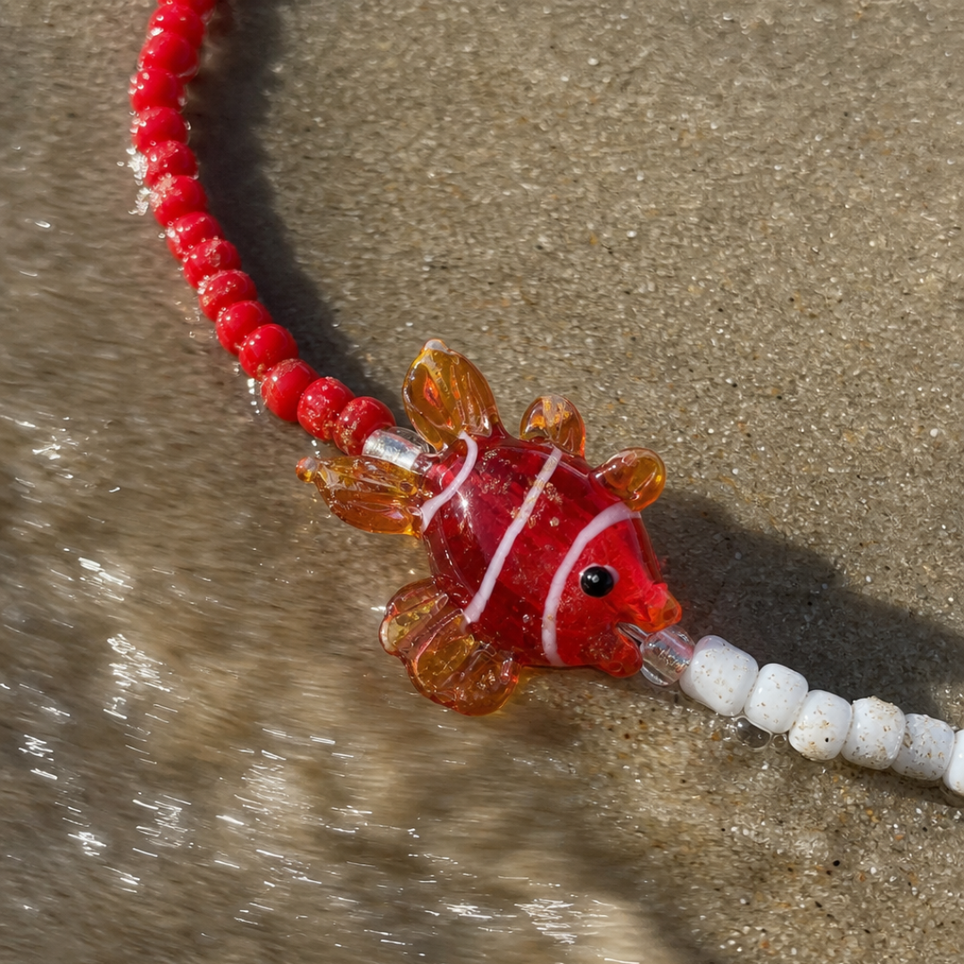 Rood-witte kralenketting met glazen vis bedel van Casa Jadel op het strand