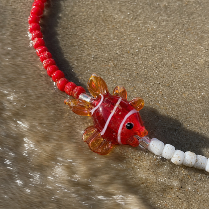 Rood-witte kralenketting met glazen vis bedel van Casa Jadel op het strand