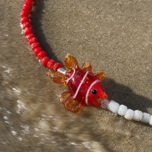Rood-witte kralenketting met glazen vis bedel van Casa Jadel op het strand