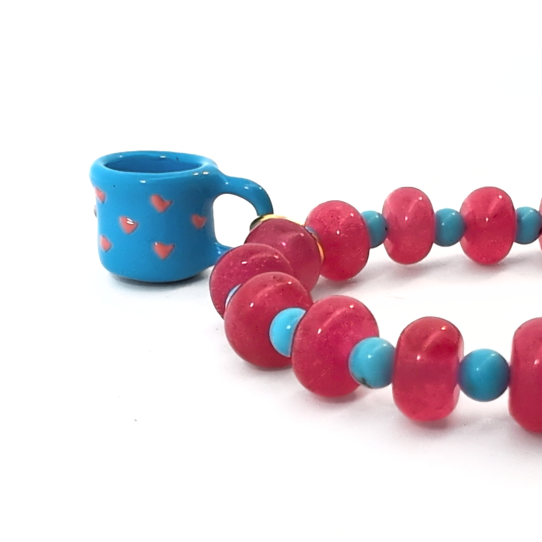 Close-up van roze glazen kralen met blauwe tussenkraaltjes en mug mokje bedel van Jadel.