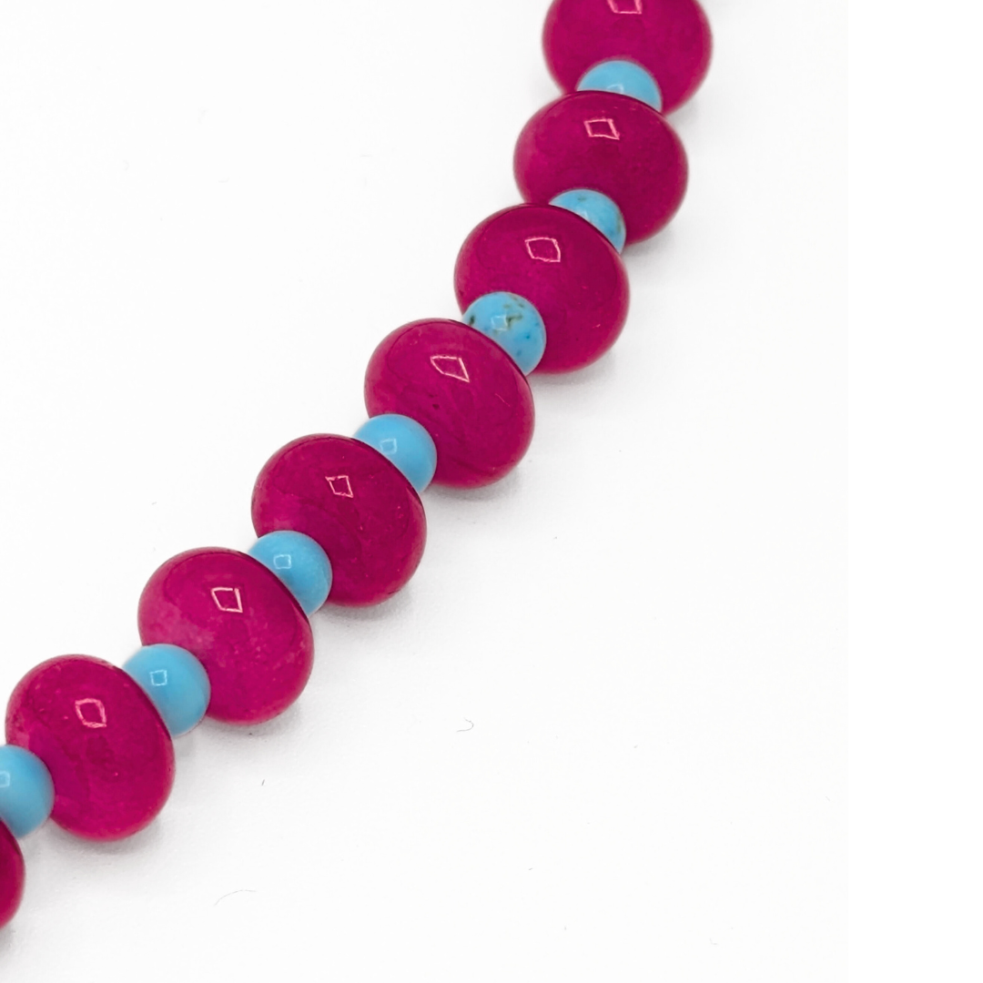 Detail van roze glazen kralenketting met blauwe kraaltjes en speels accent