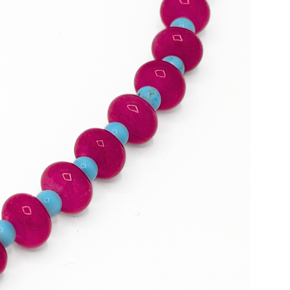 Detail van roze glazen kralenketting met blauwe kraaltjes en speels accent