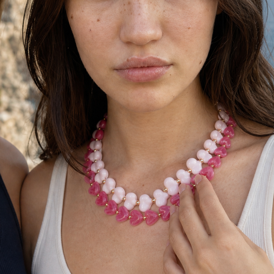 Model draagt twee roze hartjeskettingen in lichtroze en fuchsia met goudkleurige kralen van Casa Jadel
