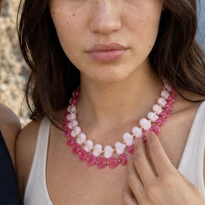 Model draagt twee roze hartjeskettingen in lichtroze en fuchsia met goudkleurige kralen van Casa Jadel
