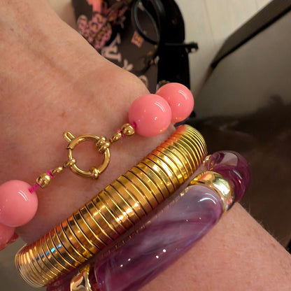 Roze kralenarmband met goudkleurig boeislot gecombineerd met gouden tube armband en paarse chunky armband, gestyled om de pols, Casa Jadel