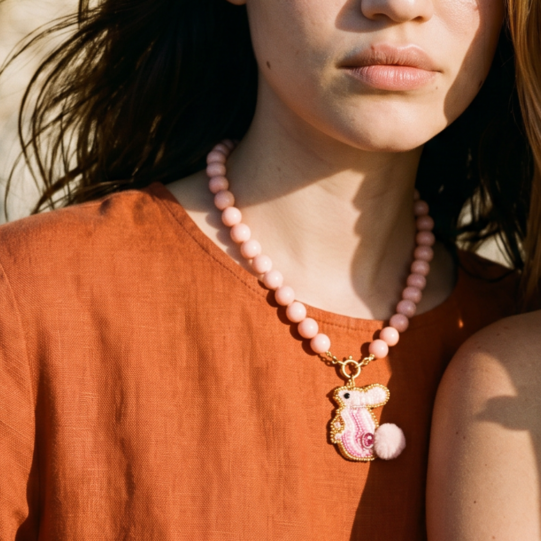 Model draagt een roze kralenketting met goudkleurige sluiting en roze zeepaard bedel van Casa Jadel