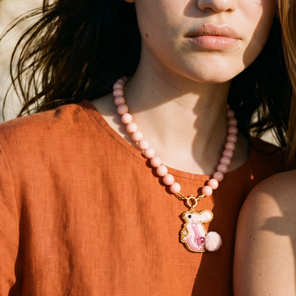 Model draagt een roze kralenketting met goudkleurige sluiting en roze zeepaard bedel van Casa Jadel