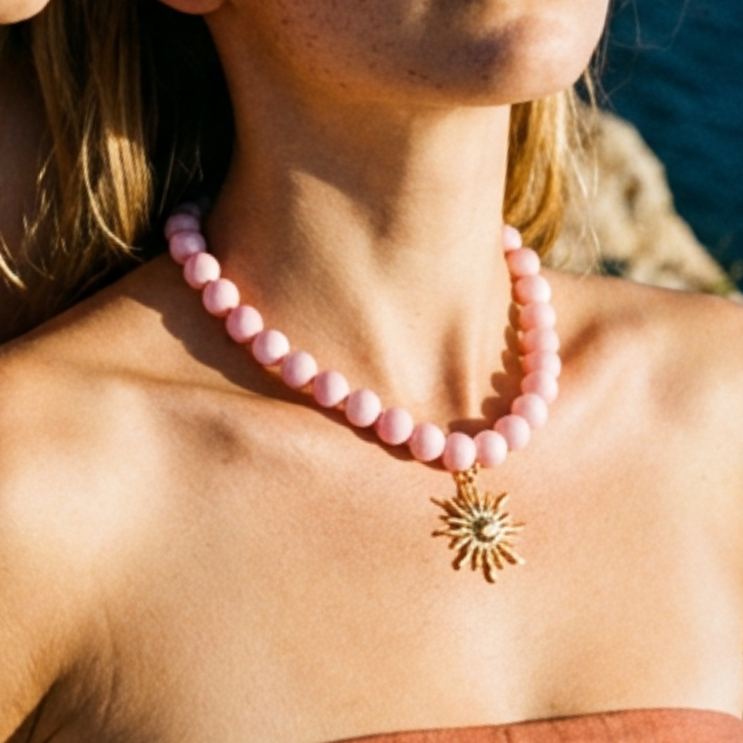 Model draagt een roze kralenketting met goudkleurige statement zon bedel van Casa Jadel